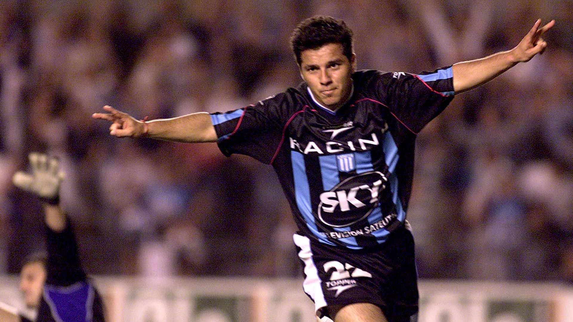 Jugador de fútbol con camiseta negra y azul, con los brazos levantados en señal de celebración.