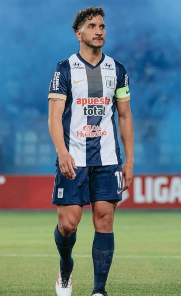 Jugador de fútbol con camiseta de rayas azul marino y blancas, de pie en un campo.