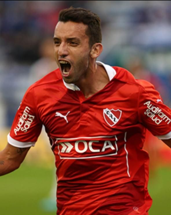 Jugador de fútbol con camiseta roja y la boca abierta, celebrando en un campo.