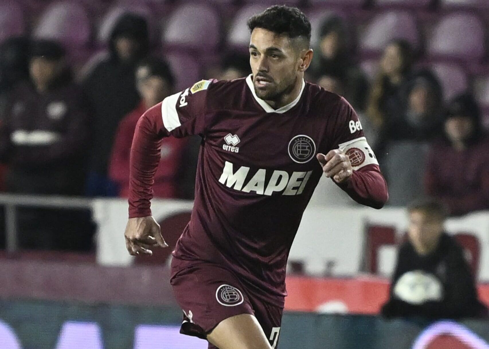 Jugador de fútbol con uniforme marrón corriendo en un campo por la noche.