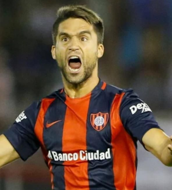 Jugador de fútbol con uniforme azul y naranja con la boca abierta en expresión de emoción.