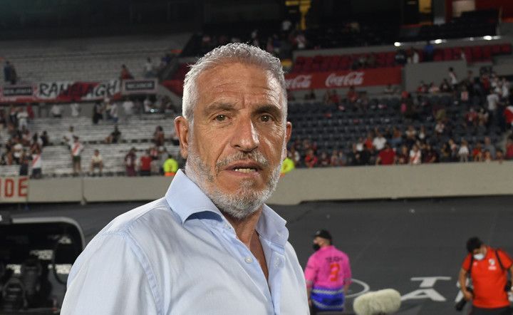 Hombre de pelo y barba grises con camiseta azul claro en un estadio de fútbol; hablando, mirando a la cámara.