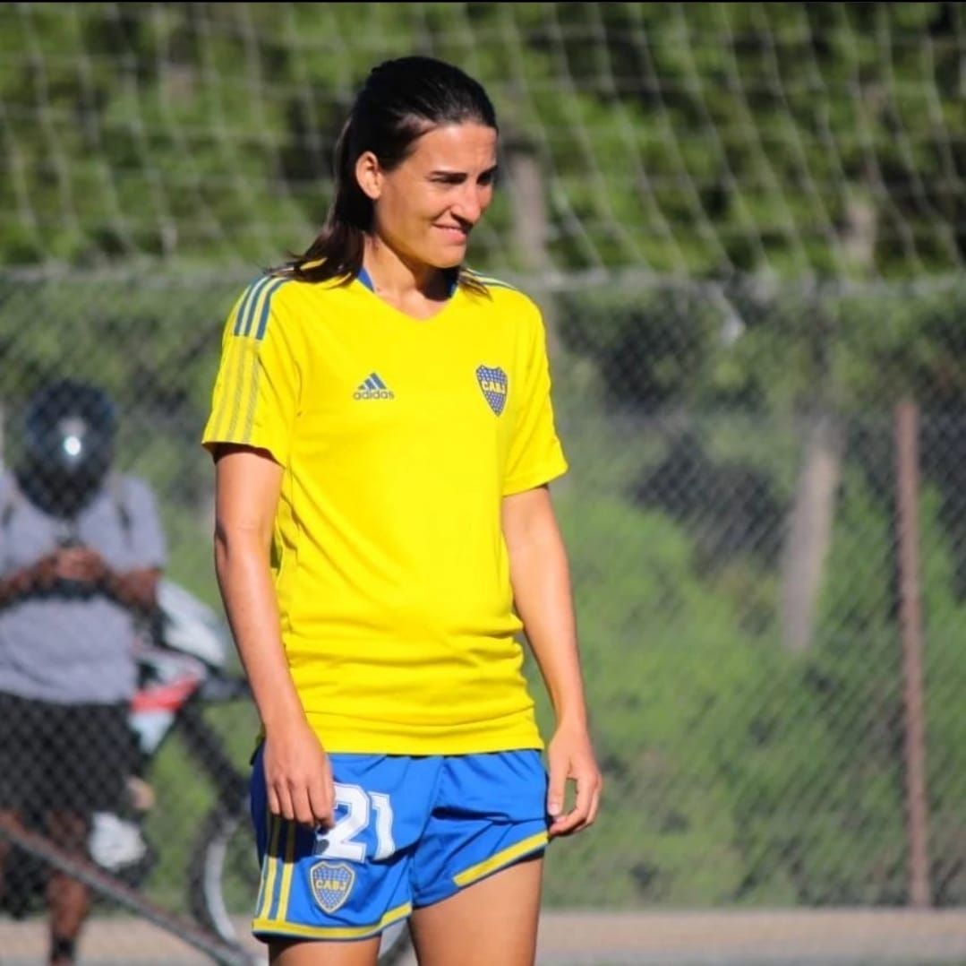 Mujer con uniforme de fútbol amarillo y azul, de pie al aire libre.