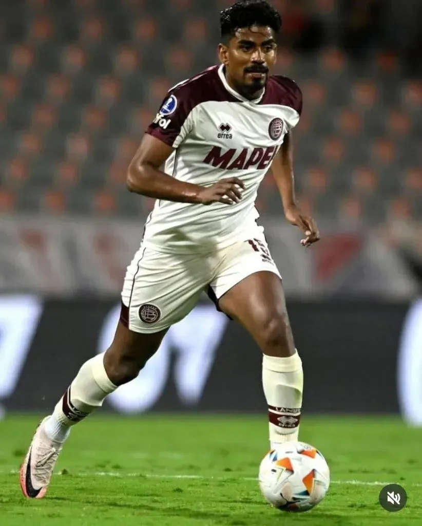 Jugador de fútbol con uniforme blanco y granate regateando un balón en un campo verde.