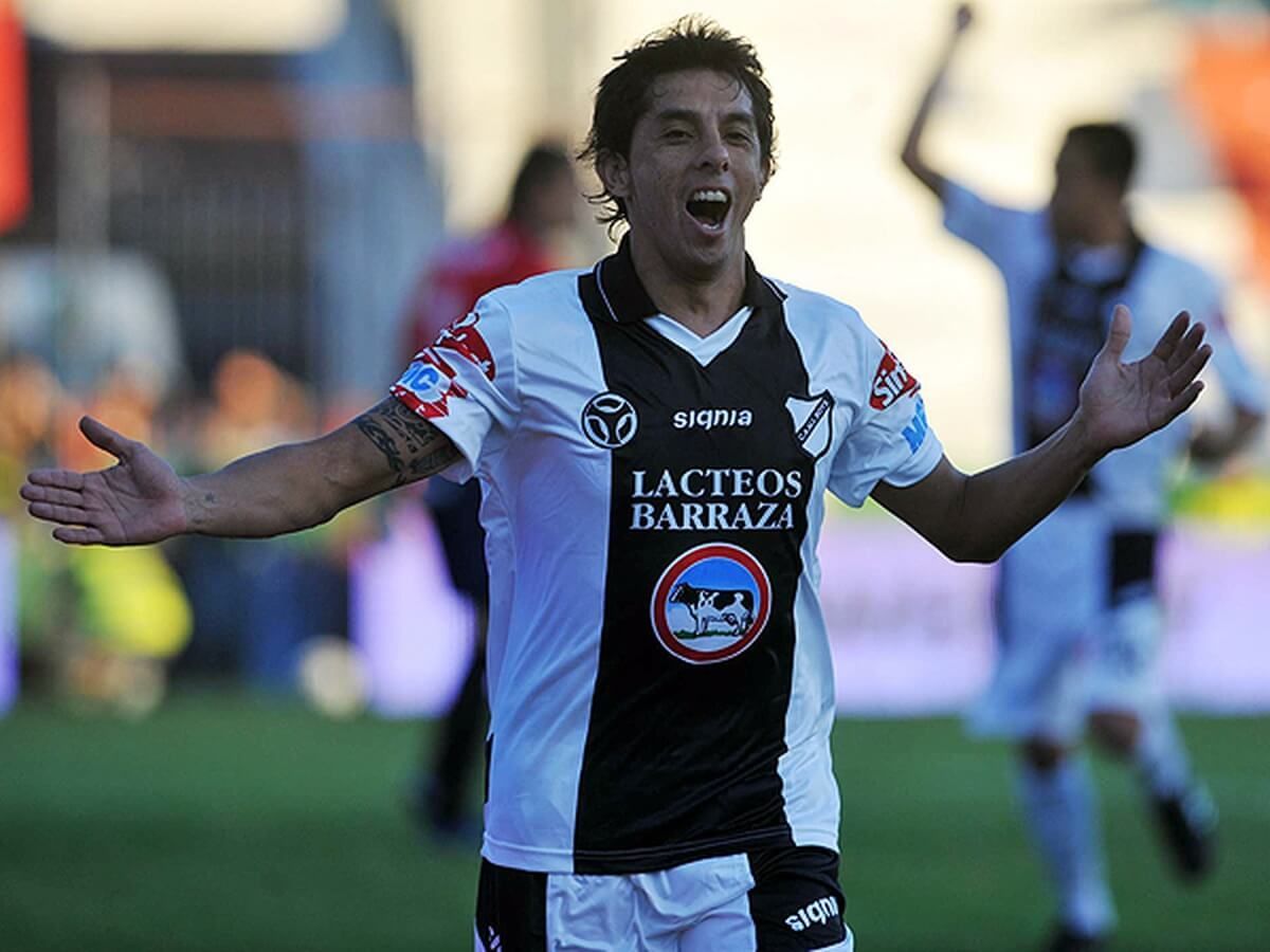 Jugador de fútbol con uniforme marrón corriendo en un campo por la noche.
