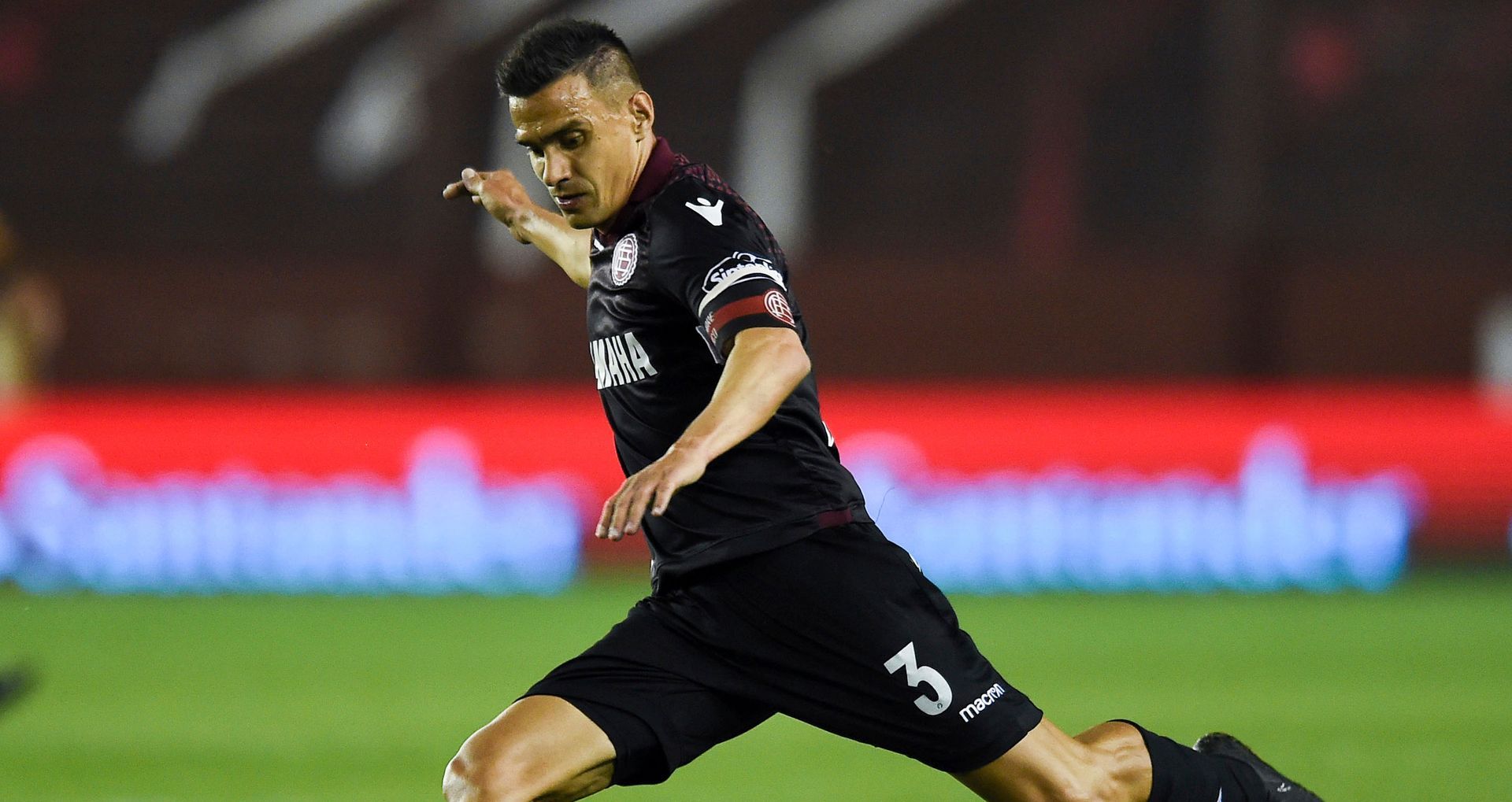 Un hombre con polo azul marino sonríe, levanta el pulgar y firma un documento con el logo del club de fondo.