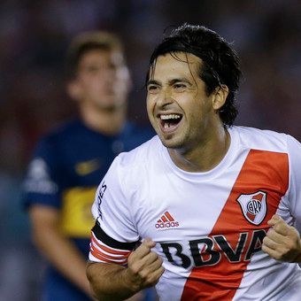 Un jugador de fútbol con camiseta blanca y roja celebra con una sonrisa y los puños en alto.