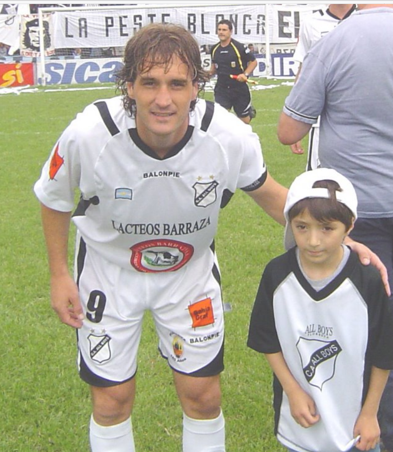 Jugador de fútbol con cabello castaño rizado con una camiseta de rayas azules y rojas, al aire libre.