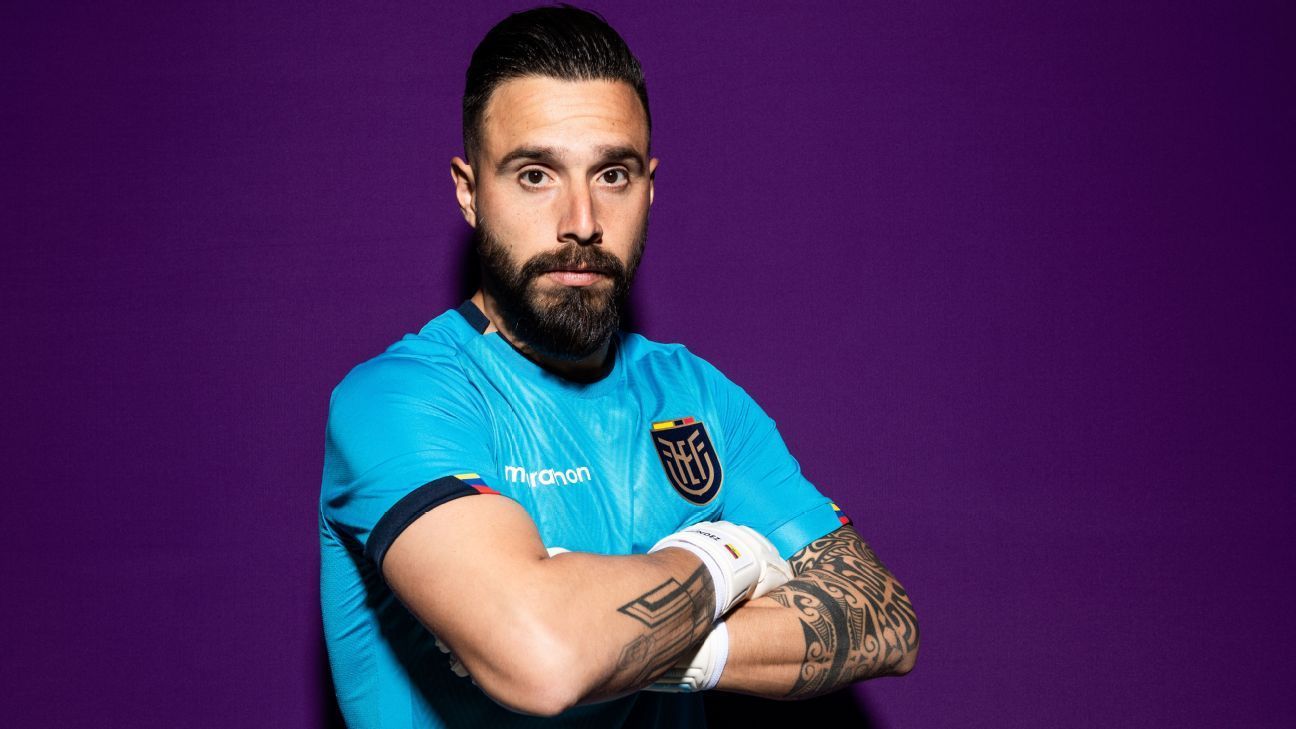 Jugador de fútbol con camiseta azul con los brazos cruzados sobre un fondo morado.