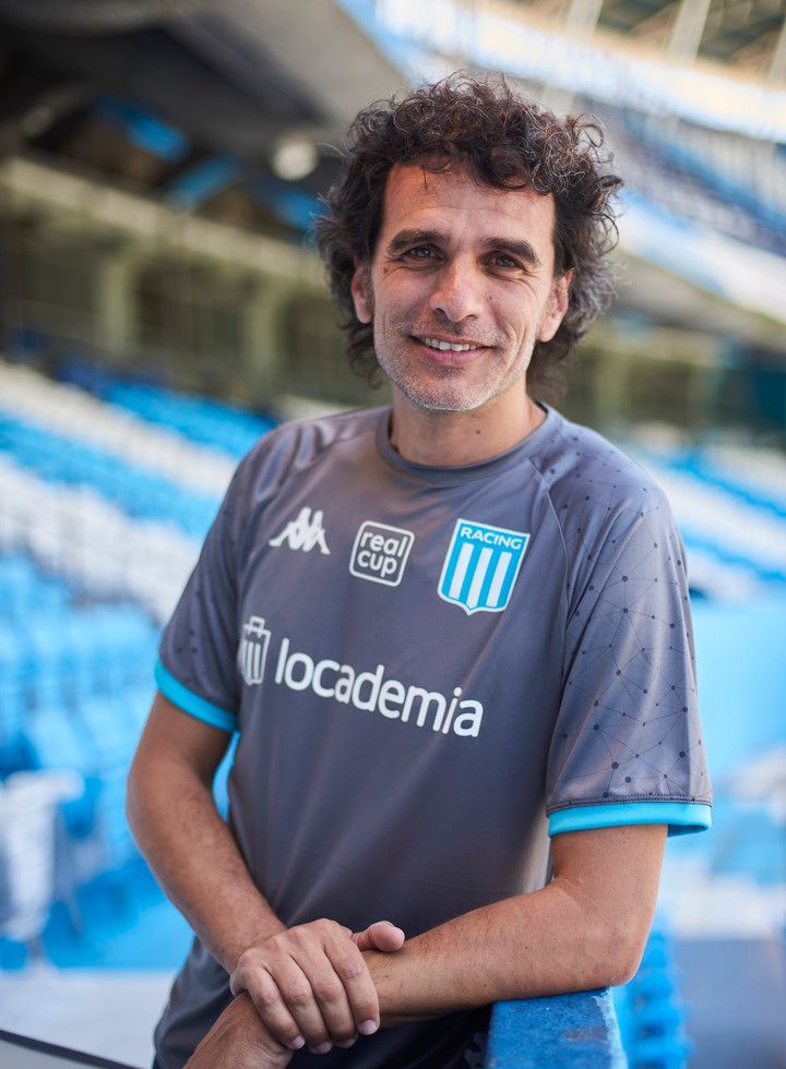 Entrenador de fútbol señalando, vistiendo chaqueta blanca, mirando el juego en el campo.