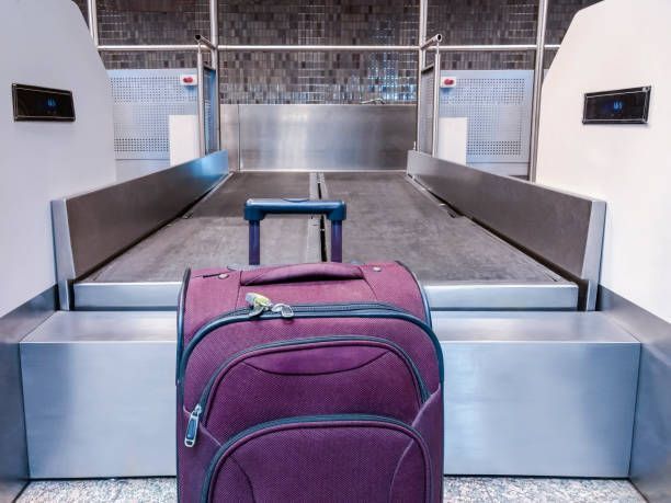 A purple suitcase is sitting on a conveyor belt at an airport.