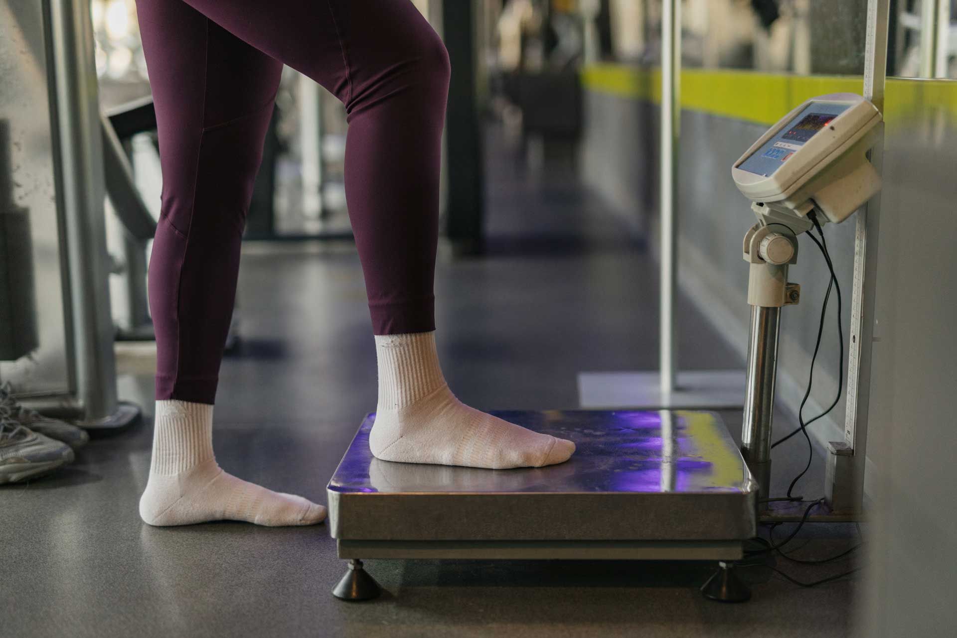 A woman is standing on a scale in a gym.
