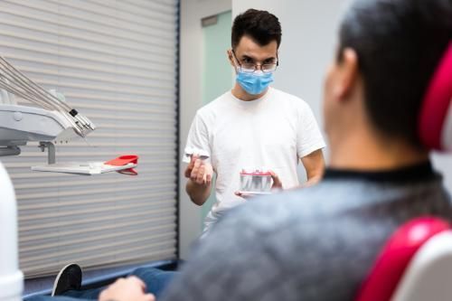 A dentist wearing a mask is talking to a patient showing a dental crown