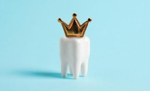 A white tooth with a gold crown on top of it on a blue background.