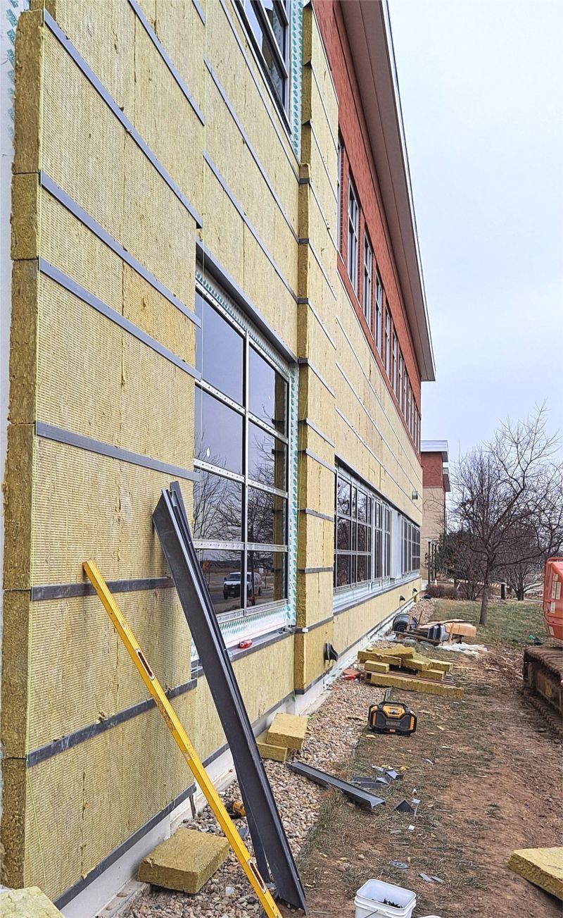 Exterior building construction with insulation panels and window installation in progress.