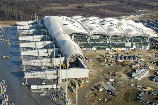 Aerial view of an airport under construction with a long, arched roof and multiple walkways.