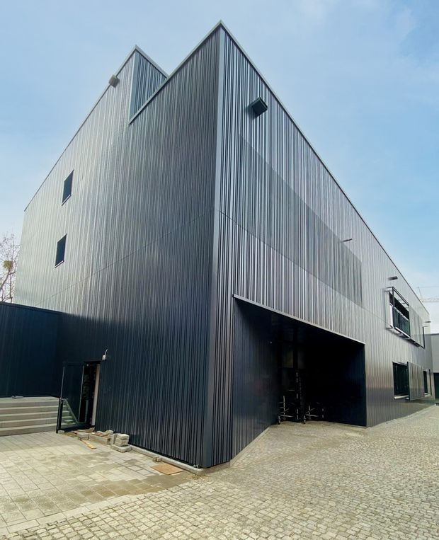 Dark gray modern building with textured facade and large entrance under a clear blue sky.