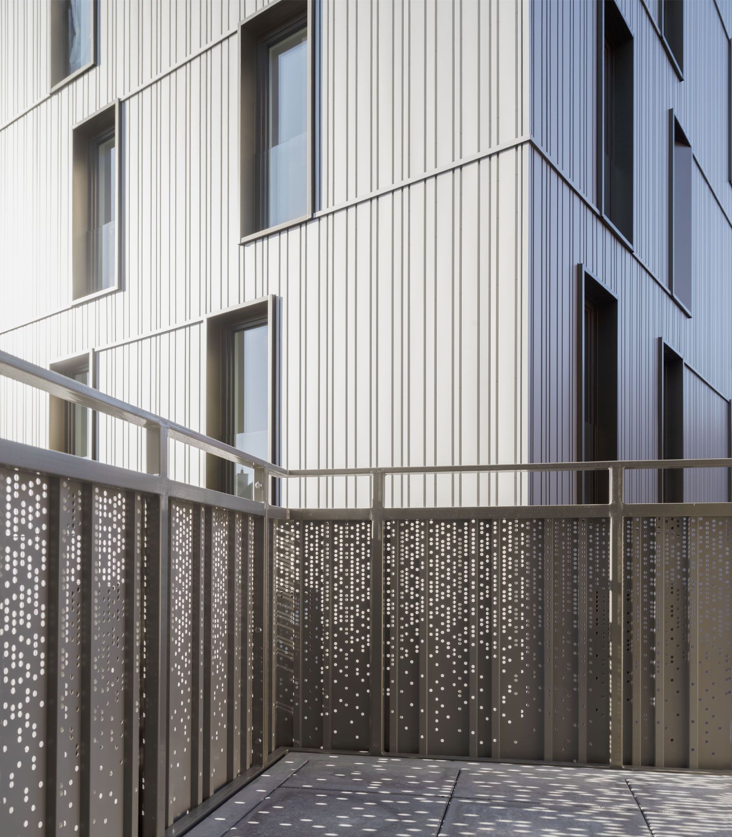 Modern building exterior with metal facade, windows, and perforated metal balcony railing.