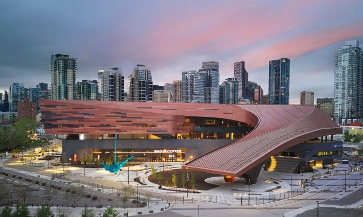 Modern library building with copper-colored facade and downtown skyline. A blue sculpture is in front.