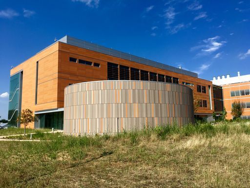 A modern brick and cylindrical building with a grassy foreground and blue sky.