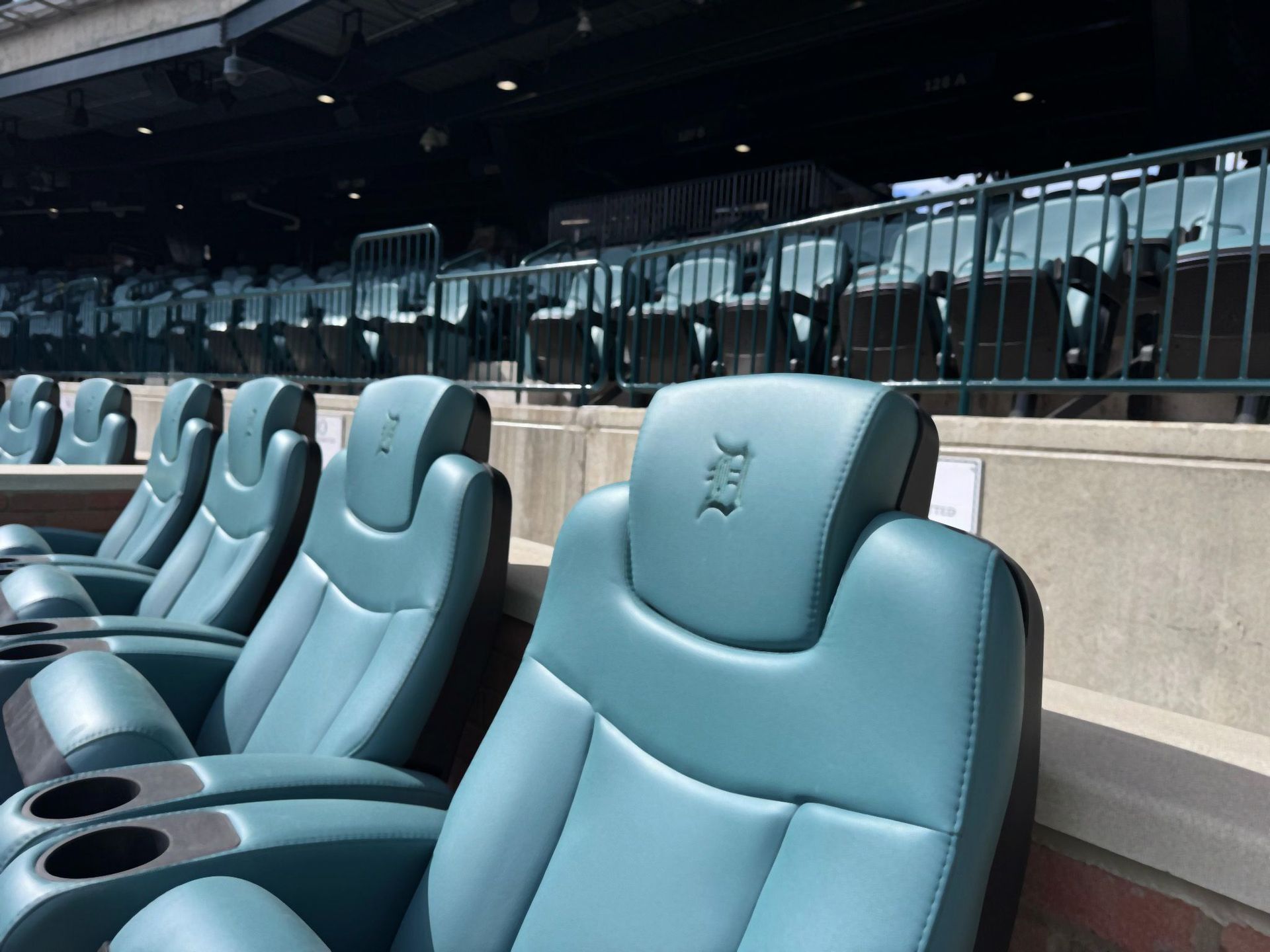 Empty teal stadium seats with cup holders; metal railings and concrete structure.