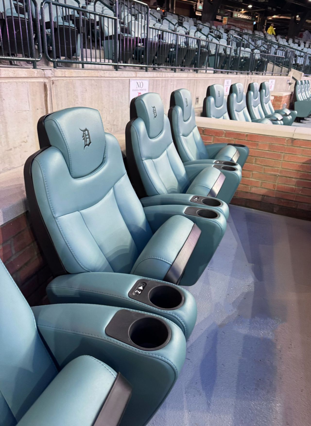Blue stadium seats with cupholders, Detroit Tigers logo on headrests, in a stadium setting.