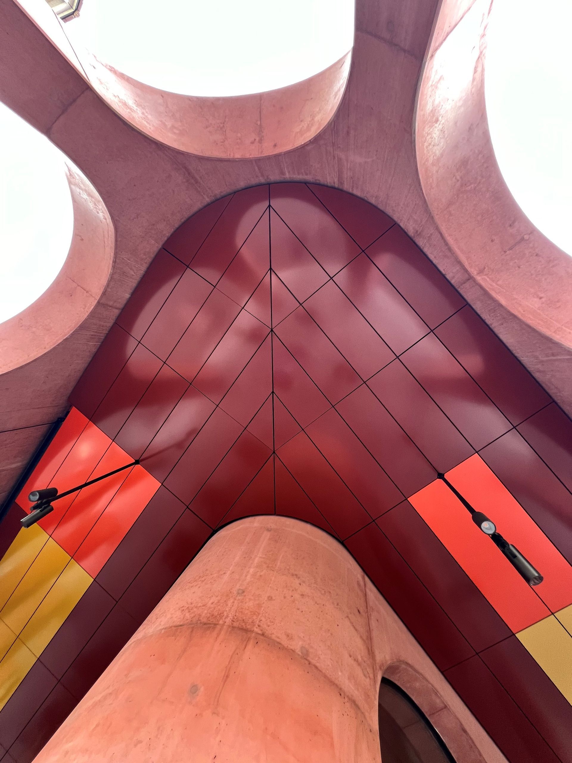 Looking up at a curved, red ceiling with round openings, two lights, and geometric dotted lines.