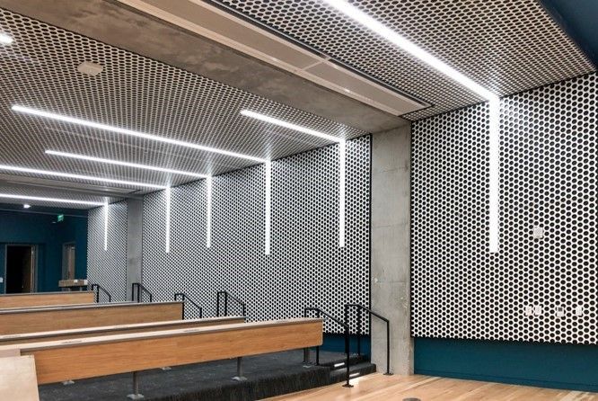 Lecture hall with geometric patterned walls and ceiling, linear lights, and tiered seating.
