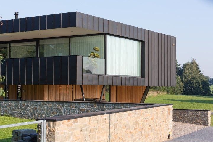 Modern home with black exterior, large window, wood accents, and stone wall.