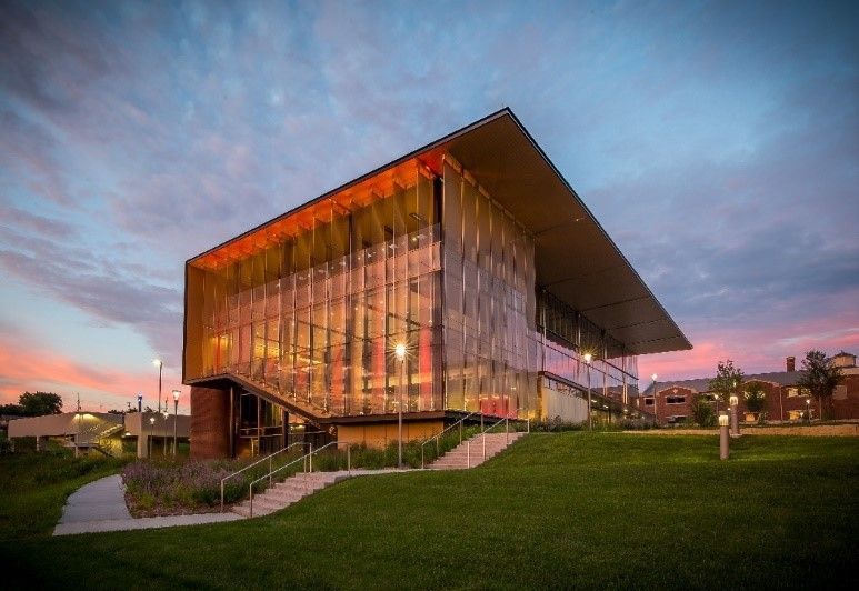 Modern building with a large overhanging roof, glass facade, and golden glow at sunset.