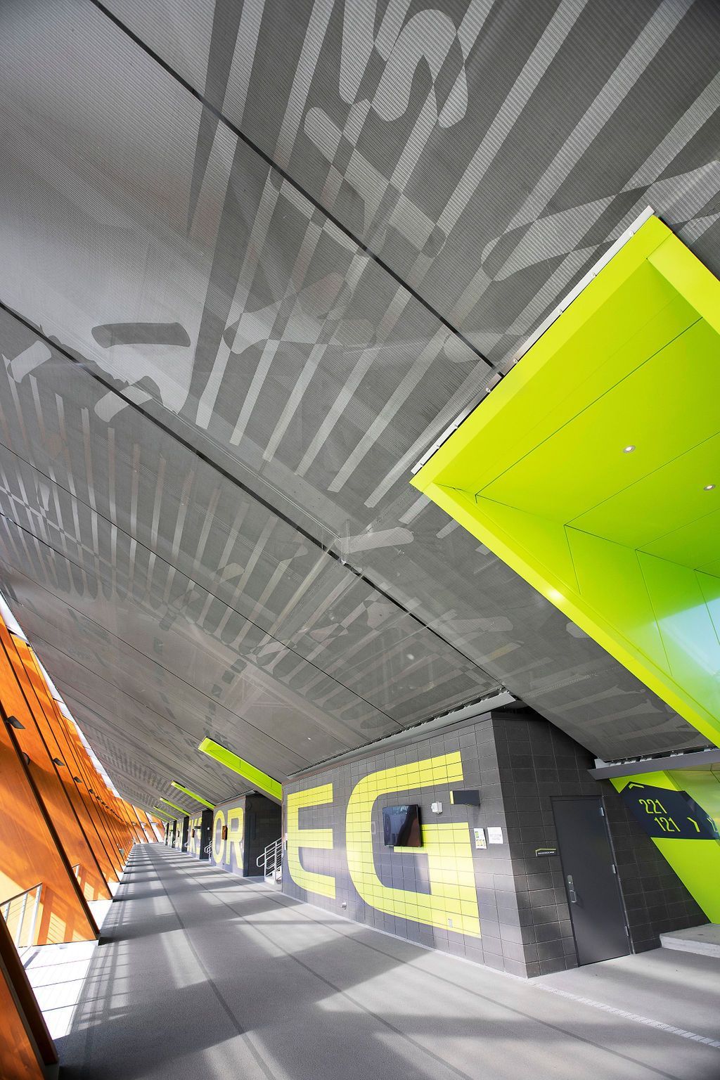 Perforated metal ceiling with text and lime green and orange accents in a modern building.