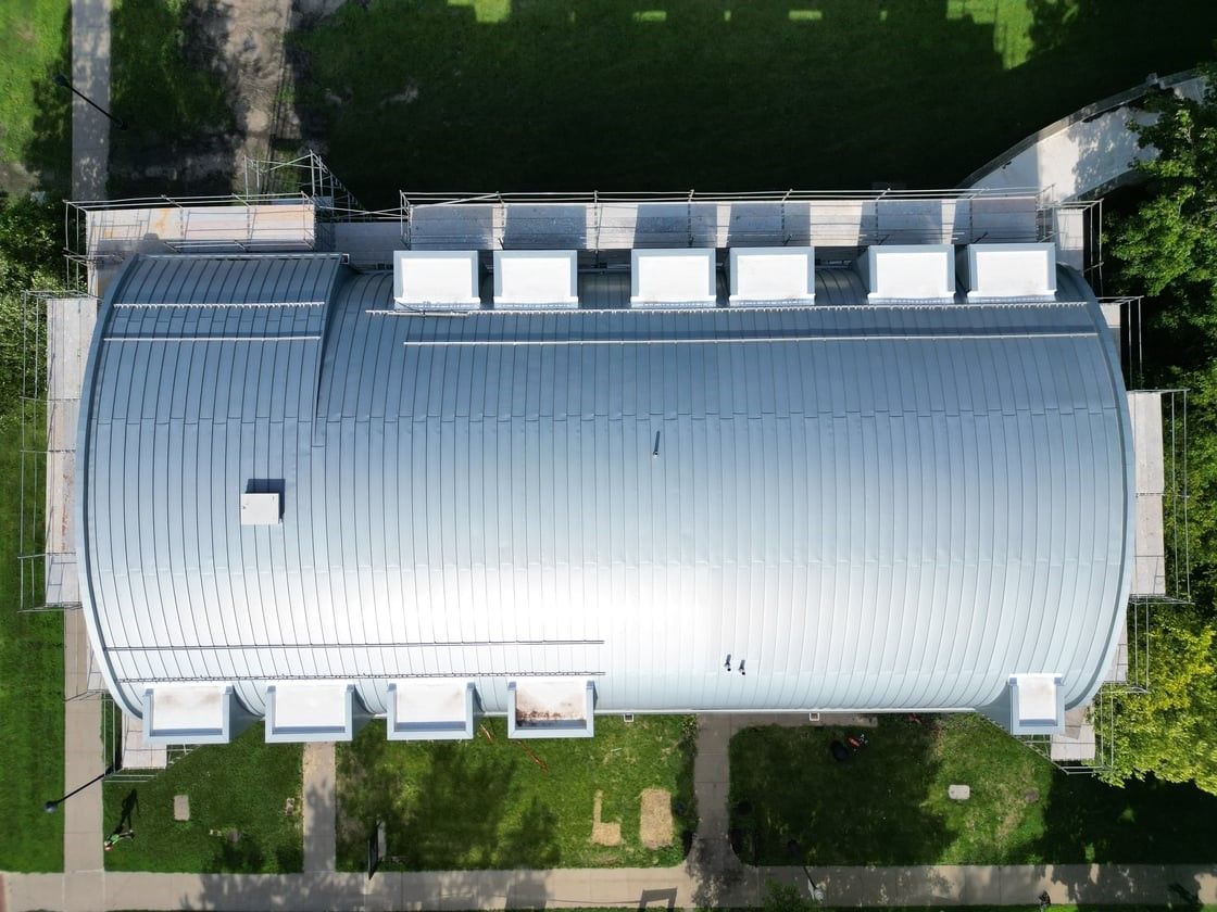 Aerial view of a metal-roofed building, surrounded by green grass and sidewalks.