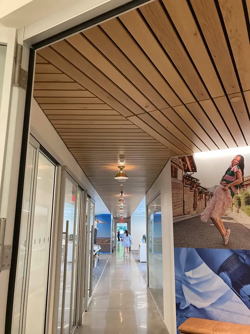 Hallway with wooden ceiling, glass walls, and a person walking towards the end.