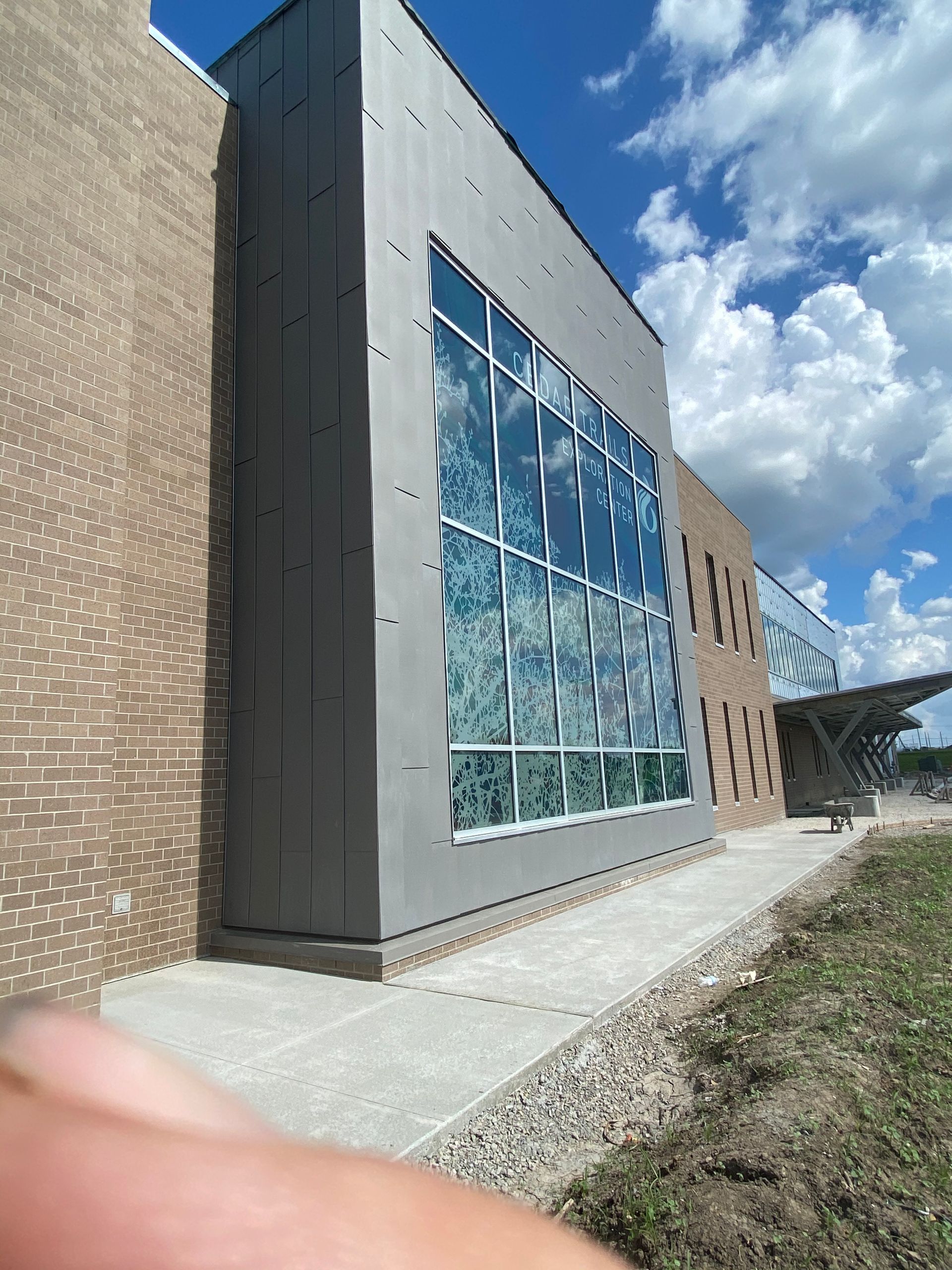 Building exterior with large glass windows reflecting blue sky and clouds. Brick and gray facade.