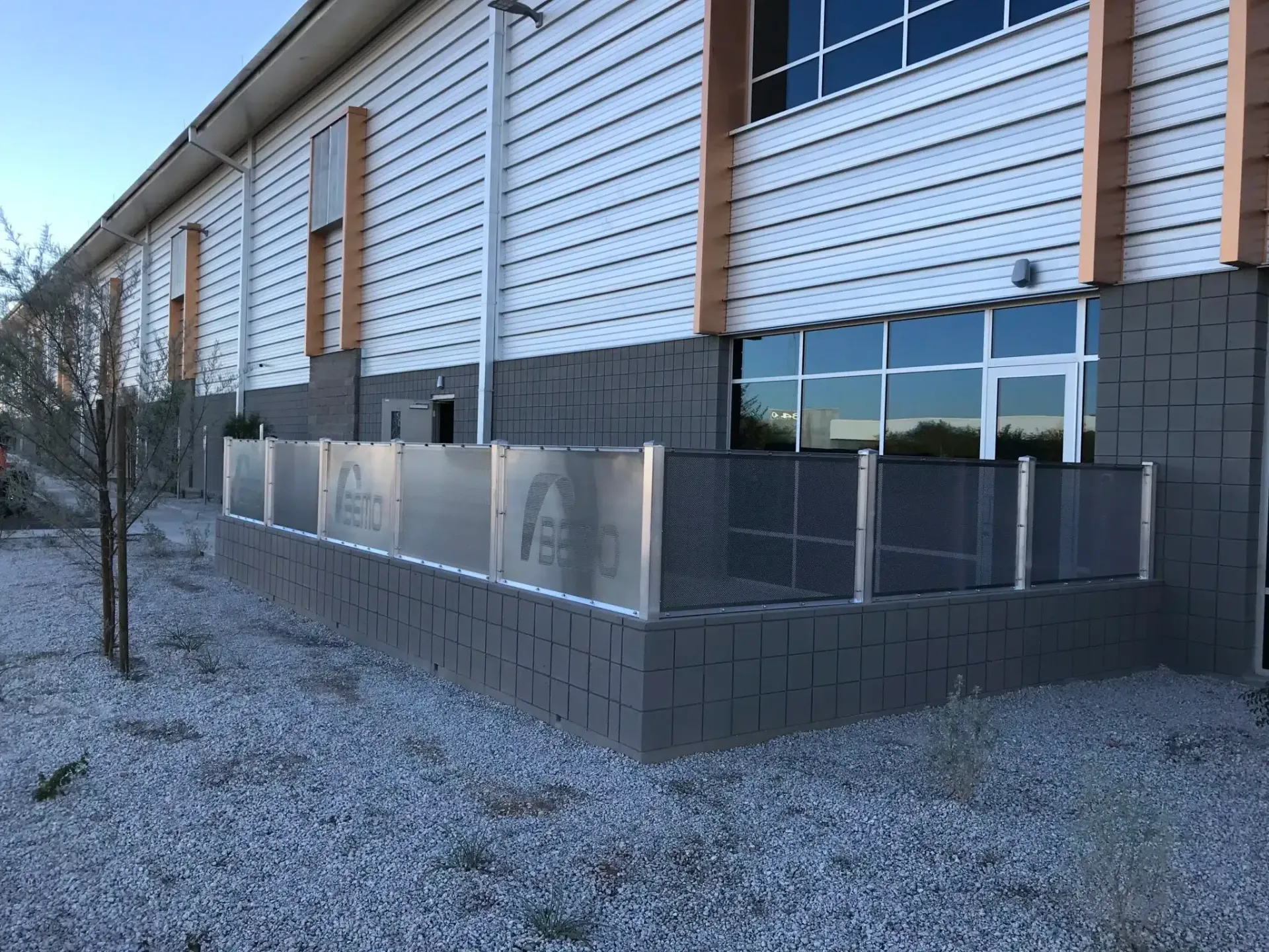 Exterior of a building with a gray facade, metal fencing, and windows.