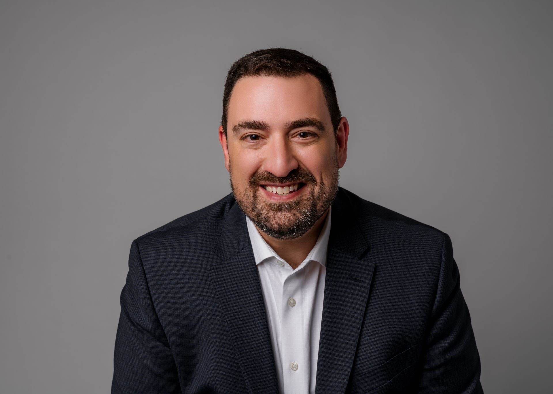 Man in a suit smiles at the camera against a gray backdrop.
