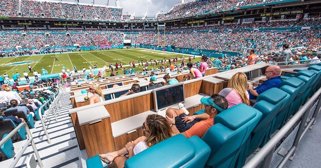 Football stadium crowd; people in turquoise seating, field in view.
