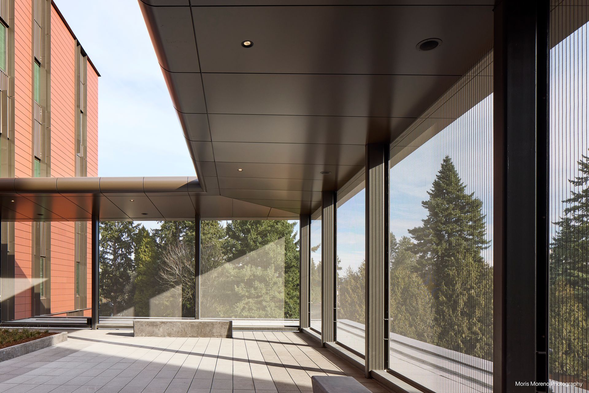 Covered walkway with glass walls, brick building, and trees visible.