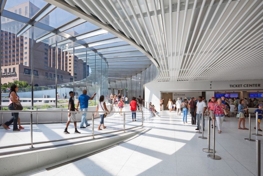 People walk through a bright, modern transit center with glass walls and a curved ceiling.