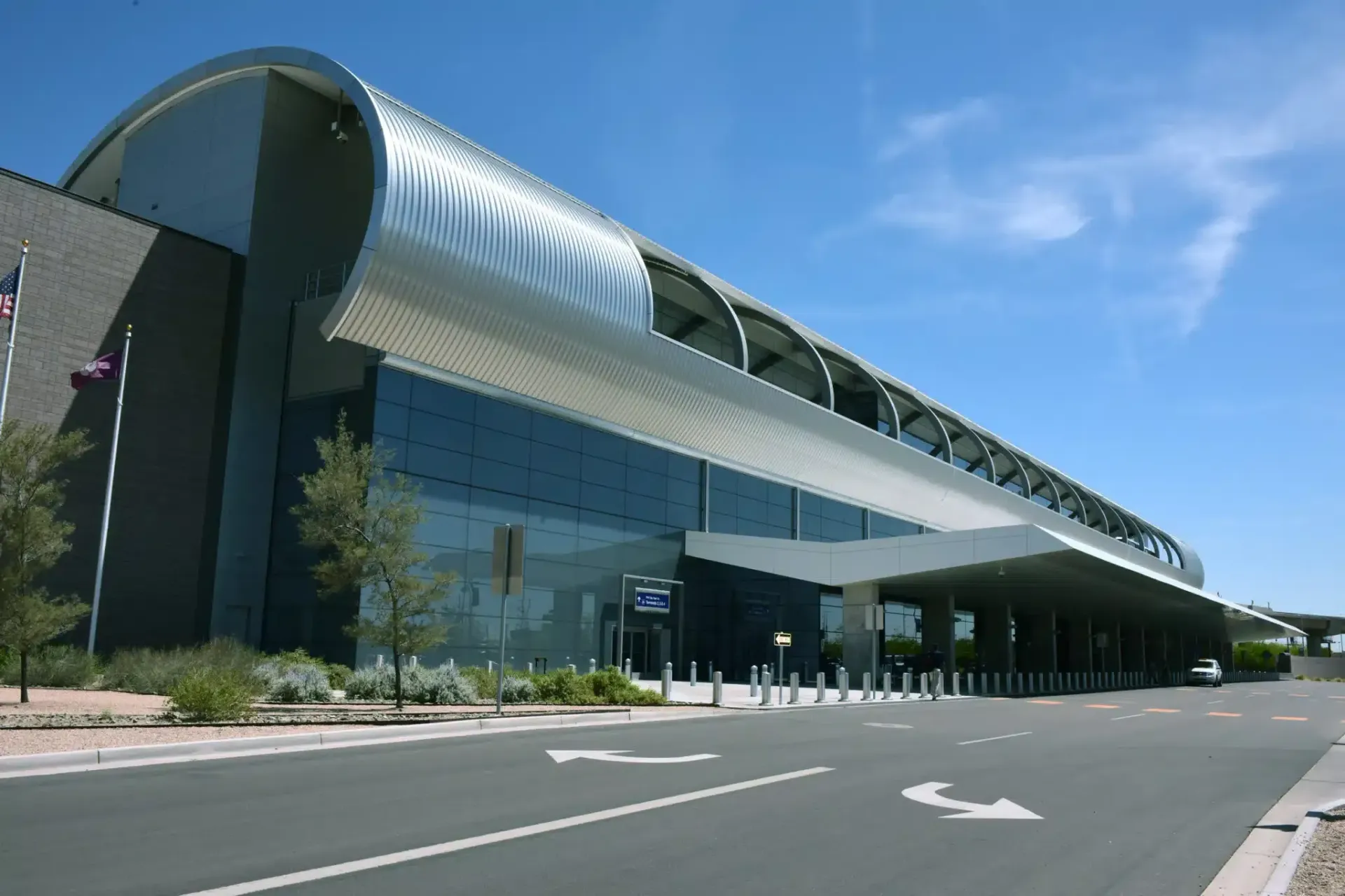 Modern airport terminal exterior with a curved silver roof and glass facade under a blue sky.