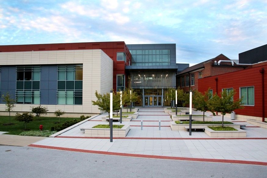 Modern brick and glass building with trees and walkway. Cloudy sky.