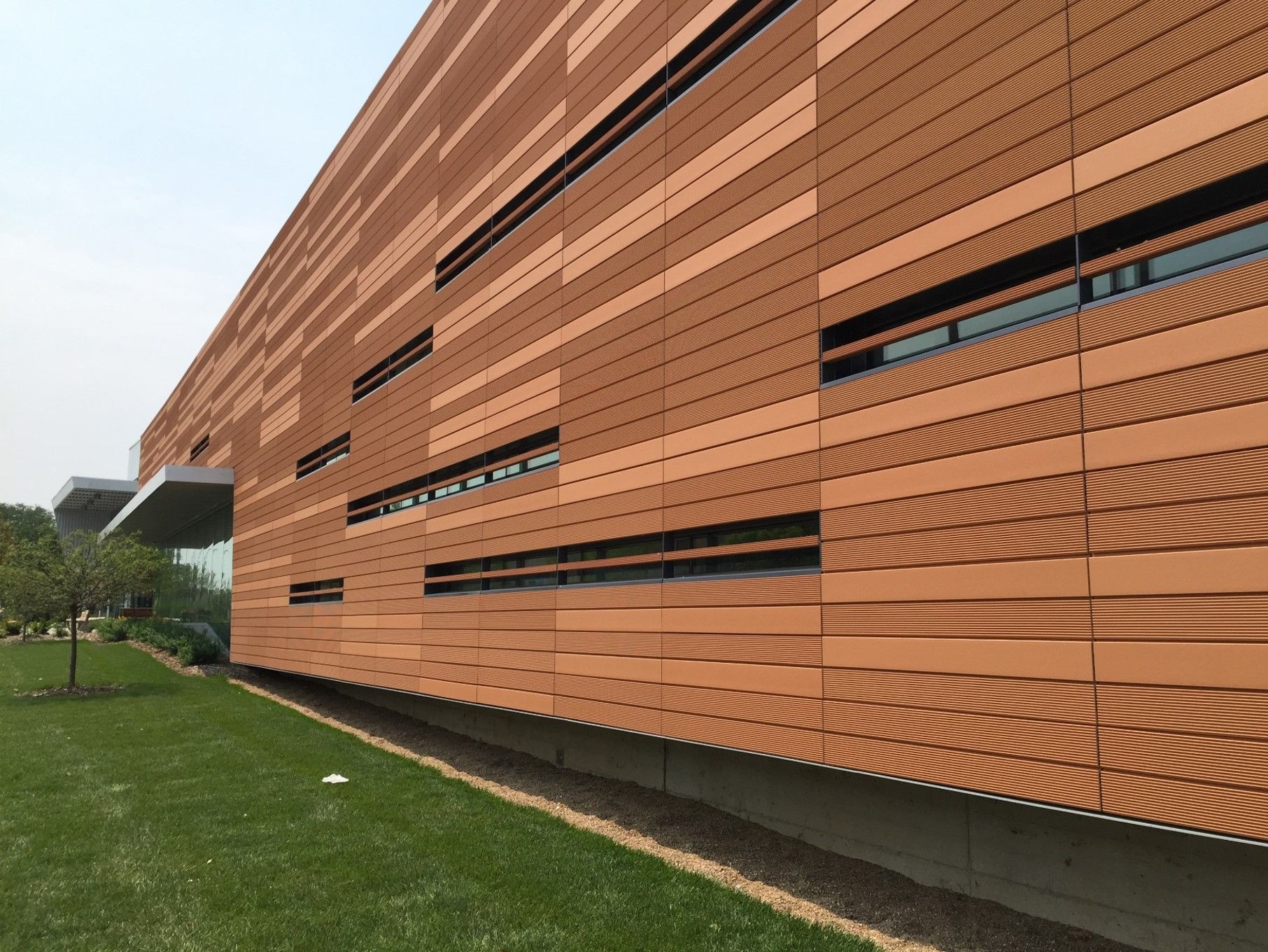 Brown and beige building with horizontal lines, black windows, and a grassy lawn.