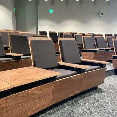 Rows of tiered wood and upholstered seating in a lecture hall. Each seat has an attached desk.