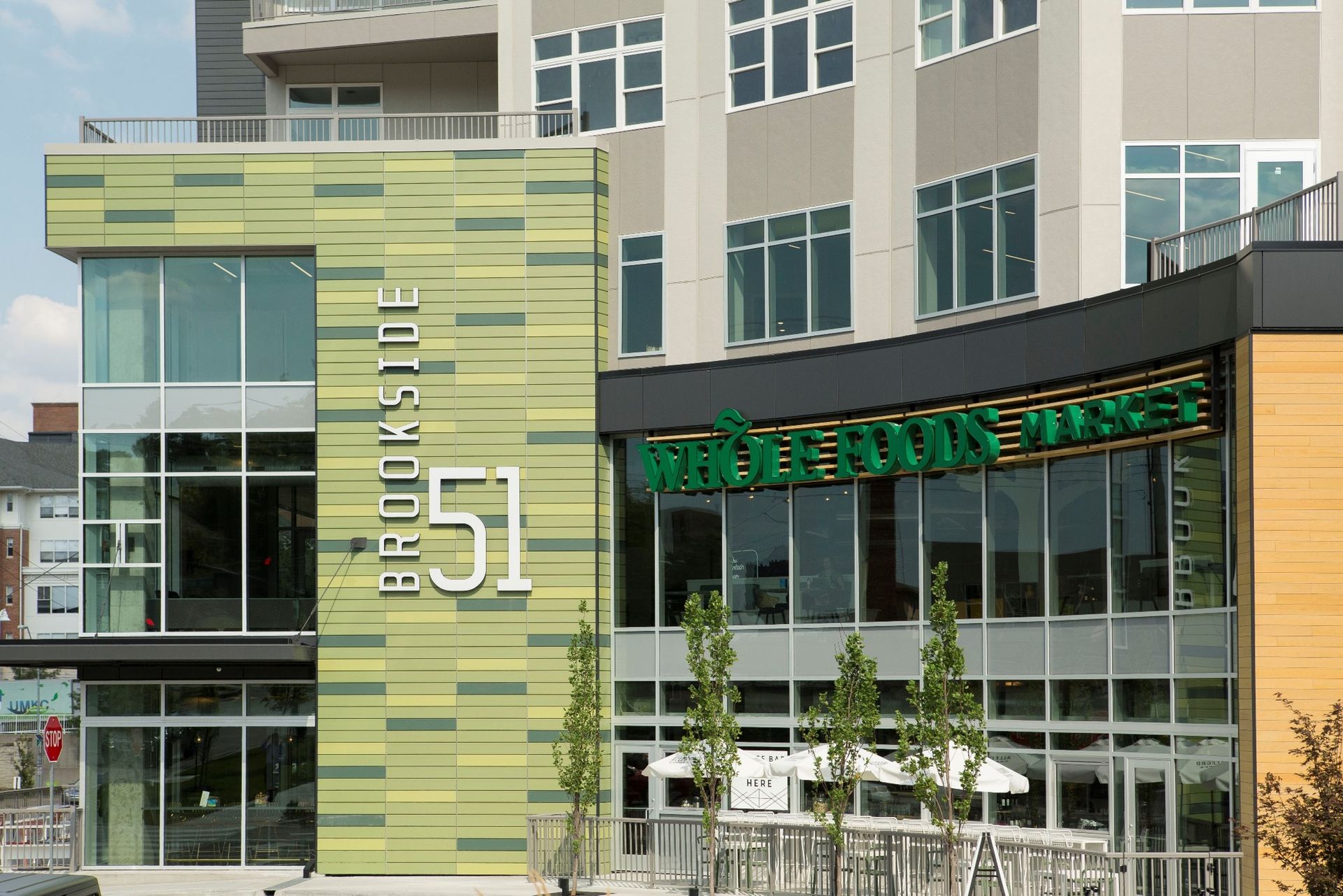 Brookside 51 building with Whole Foods Market sign. Green, gray, and tan facade with large windows, sunny day.