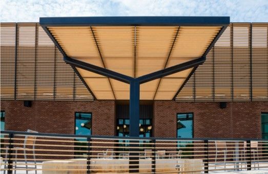 Modern building entrance with a shade structure, brick facade, and blue windows.