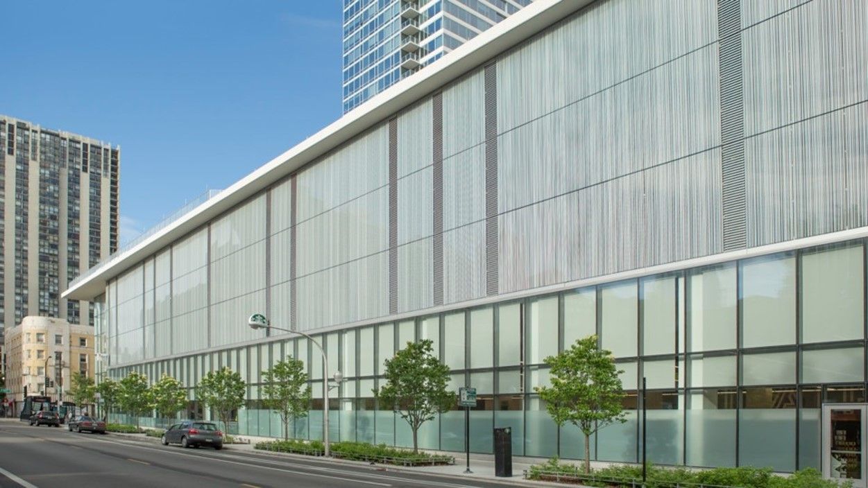 Modern building with glass panels and a tree-lined street.