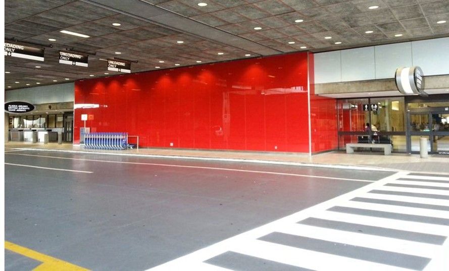 Red wall and crosswalk at an airport entrance. Blue luggage carts are parked nearby.