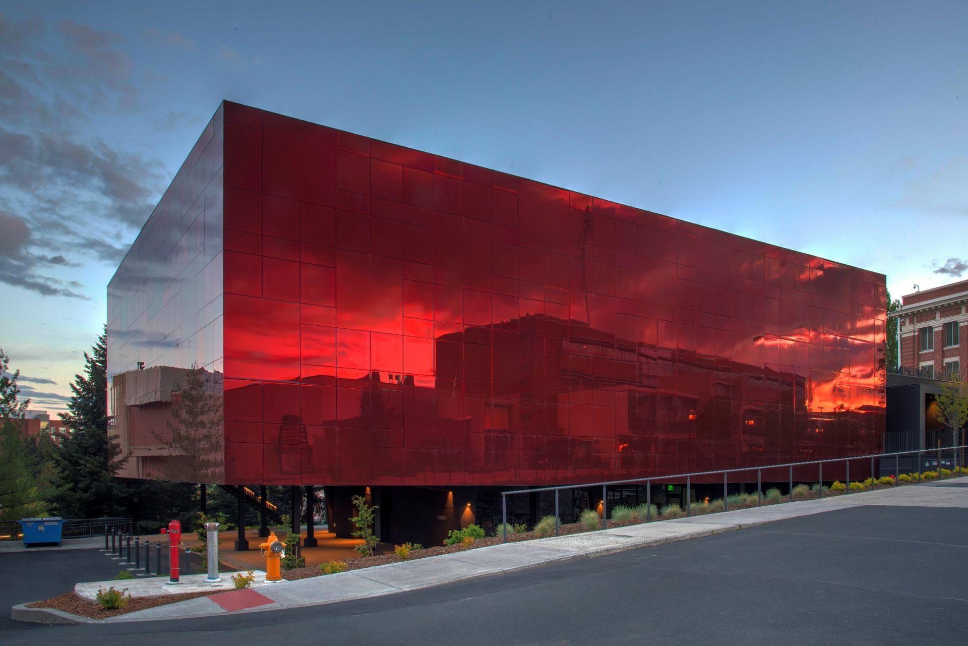 Red mirrored building reflecting a sunset and other buildings.