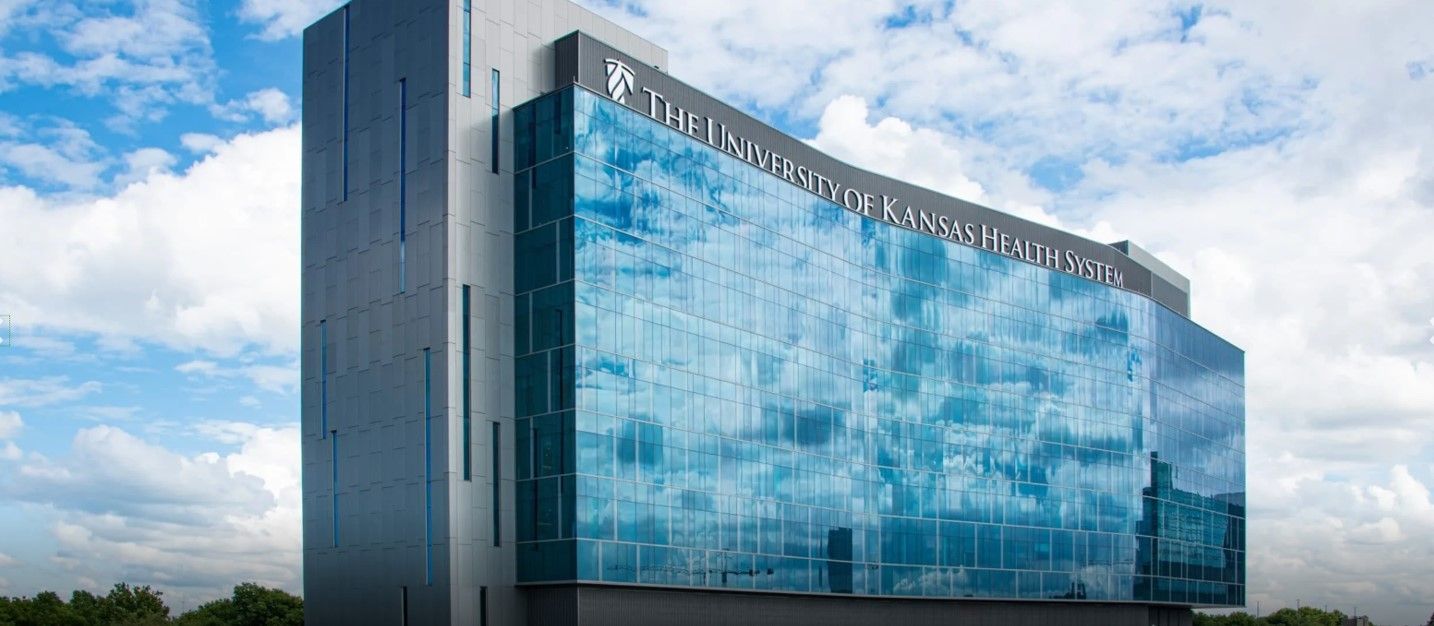 Modern glass-fronted building with a curved facade reflecting a cloudy sky.