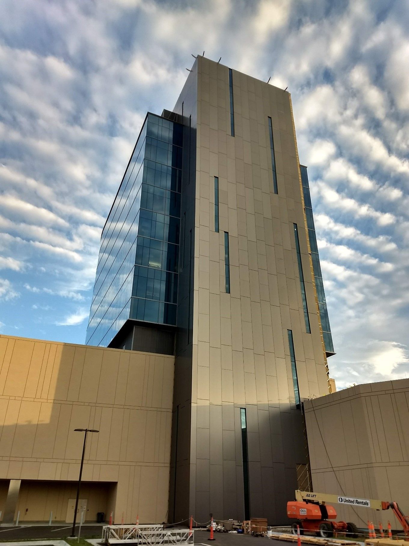 Modern high-rise building with a glass facade against a cloudy sky; construction equipment in foreground.